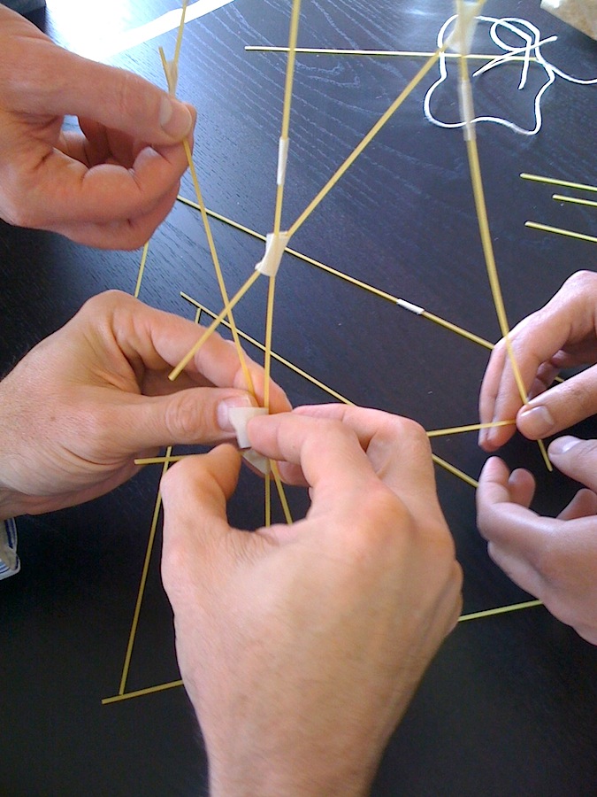 A closeup of hands working with dried spaghetti and tape