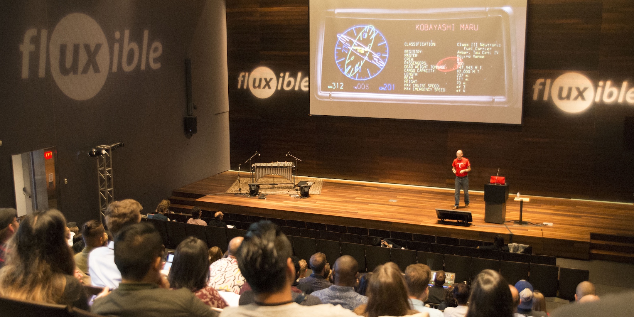 A person on a stage in front of a sceen showing a presentation