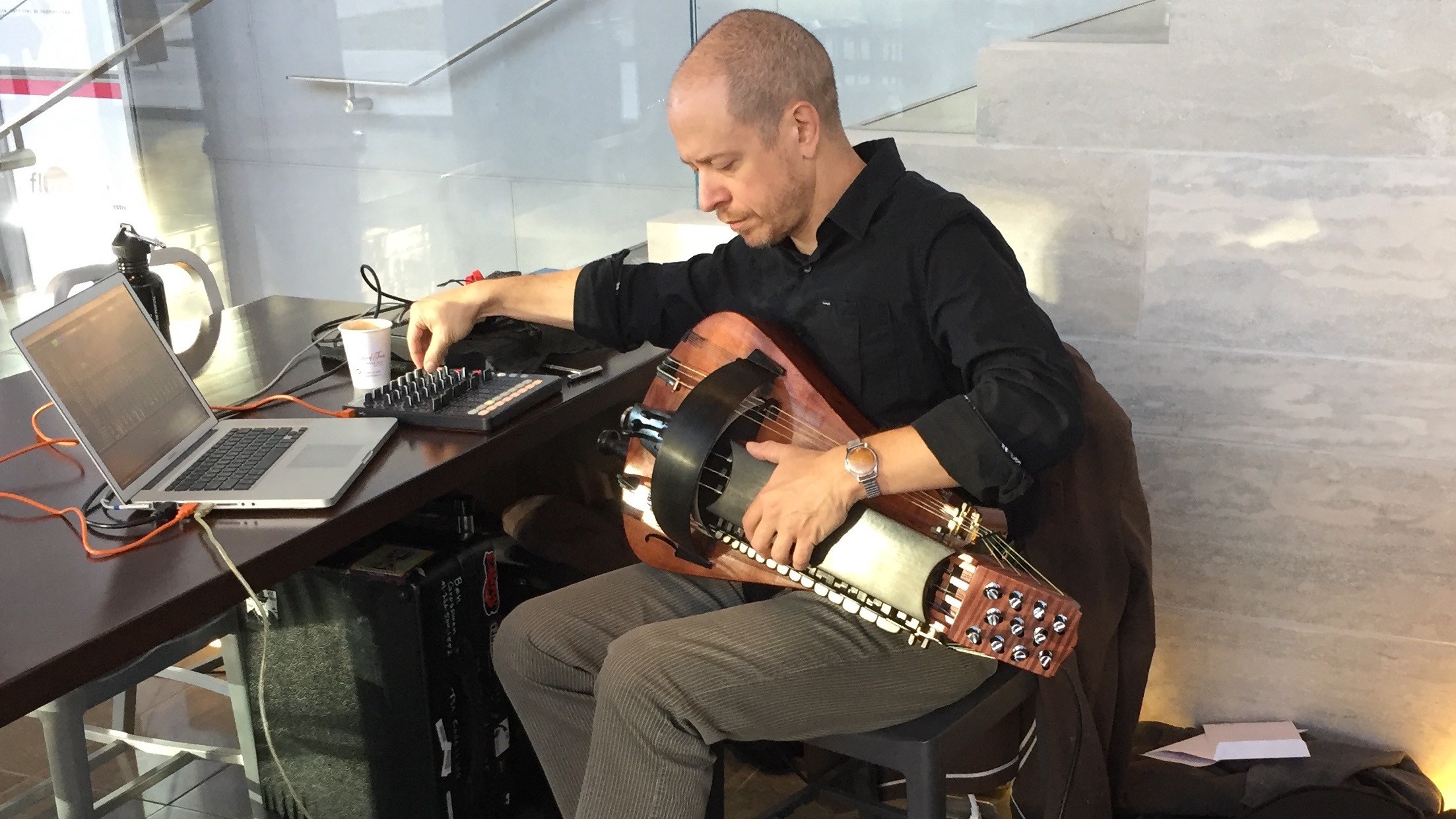 A person holding a hurdy gurdy while manipulating hardware controls on a table top
