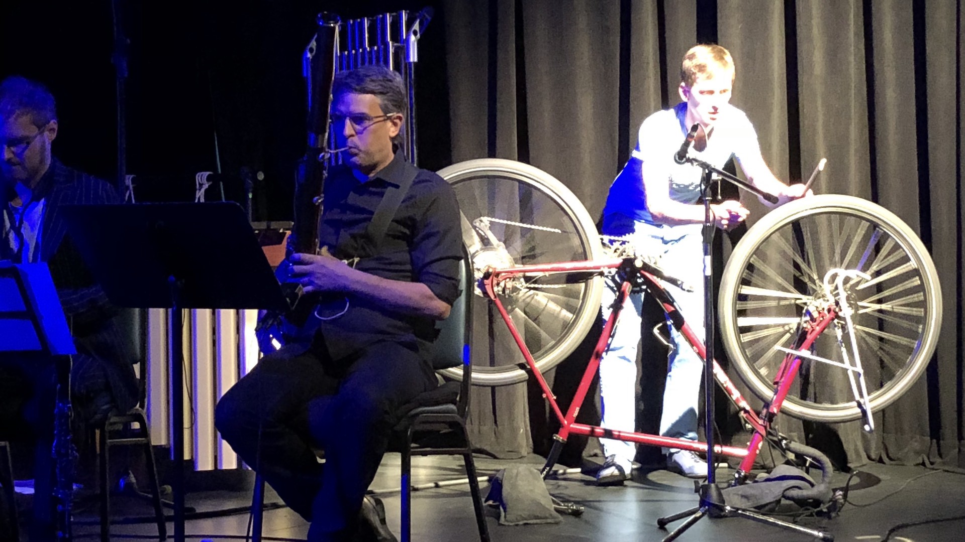 A percissionist hitting an upside-down bicycle on a stage